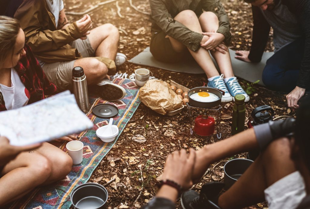 several adults sitting in the woods talking with breakfast foods