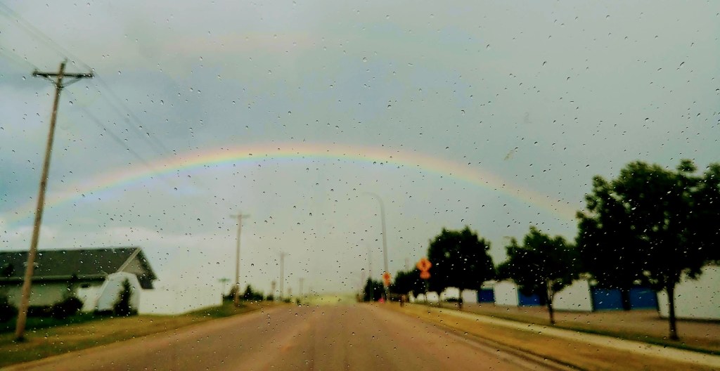 Rainbow over a tree lined road in a small town with raindrops