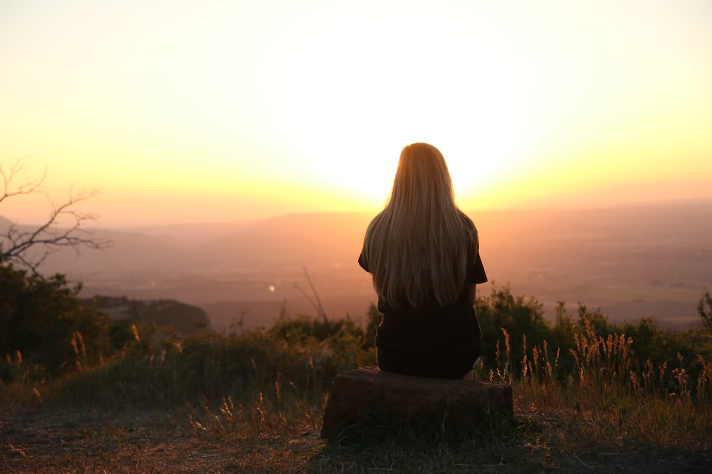 young woman sitting on tree stump overlooking lake at sunset