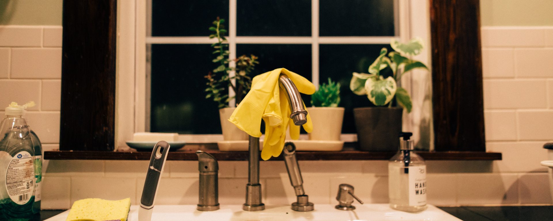 Kitchen sink in front of window with yellow gloves and sponges