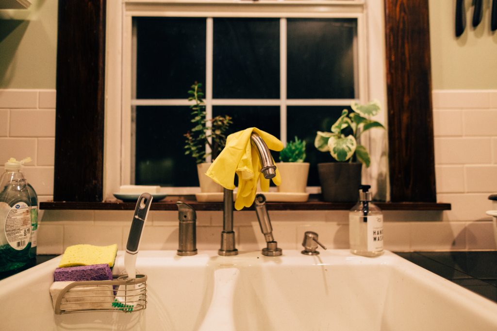 Kitchen sink in front of window with yellow gloves and sponges