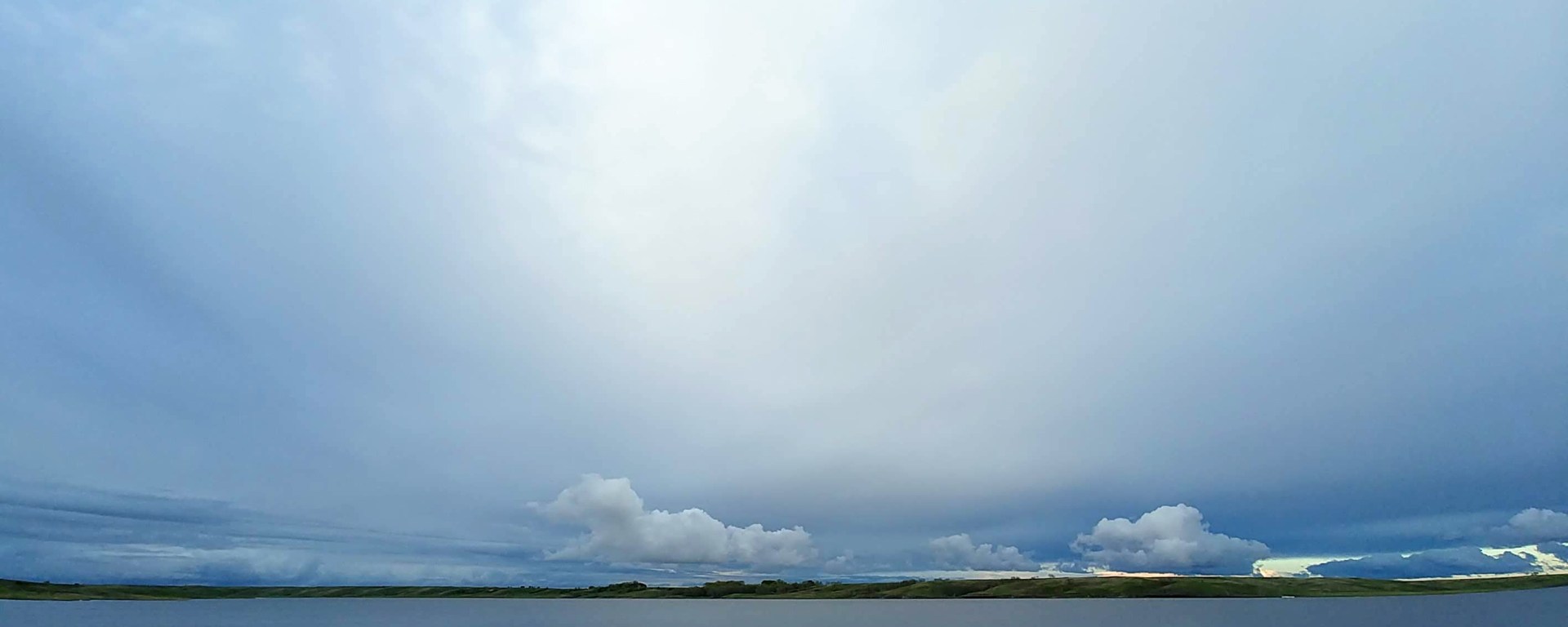 sandy beach and boat dock with rolling hills and clouds across the lake
