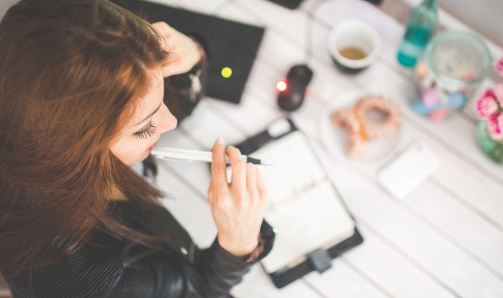 Young woman at desk with pen in mouth