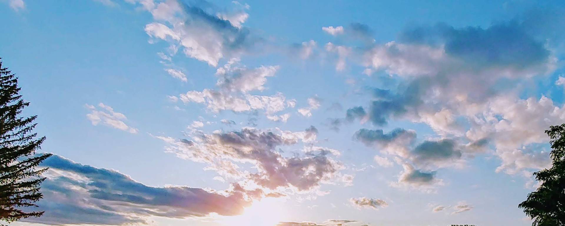Sun shining through the clouds and trees across lake